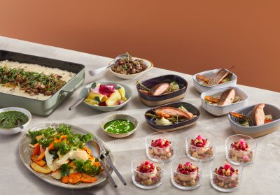 Erilaisissa astioissa ja kipoissa on lounaspöydän antimia; lohiannoksia, sienirisottoa, juureksia sekä jälkiruokaa laseissa.